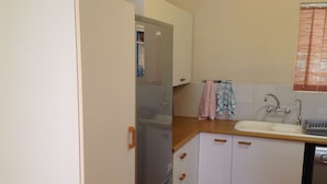 A compact kitchen with a refrigerator, a sink, and white cabinets with wooden handles.