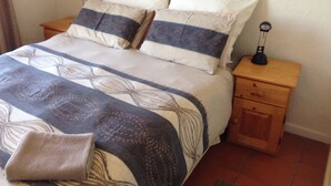 A neatly made bed with a patterned bedspread and pillows, a bedside table with a lamp, and a wooden nightstand with a drawer.