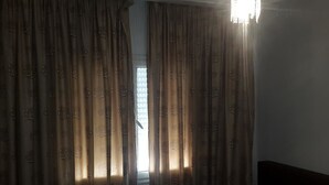 Ein Zimmer mit einem Bett, einem Vorhangfenster und einer Leuchte.