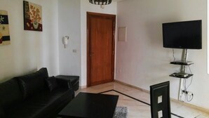 A living room with a black sofa, a coffee table, a TV on a stand, and a door. - El hana apartments (Kalaat El Andalous)