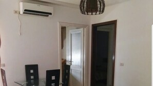 A dining area with a glass table and chairs, a black sofa, and a black coffee table. There is a ceiling light fixture and an air conditioning unit on the wall. - El hana apartments (Kalaat El Andalous)