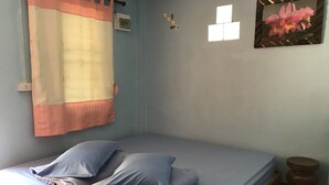 A single bed with a grey mattress and pillows, a wall-mounted air conditioner, a small framed picture, and a wooden stool. - Phusawantawansuay Resort (Thoeng)
