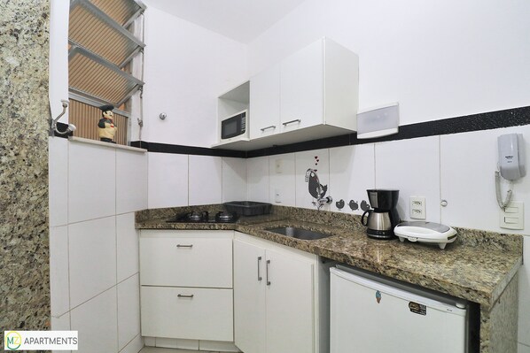 A kitchen with white cabinets, a granite countertop, a microwave, a coffee maker, and a scale. - MZapartments Prado LB301 (Rio de Janeiro)