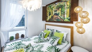 Un dormitorio con cama, ventana con cortinas, un cuadro y una lámpara de pared.