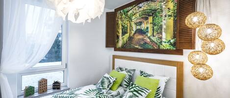 Un dormitorio con cama, ventana con cortinas, un cuadro y una lámpara de pared.