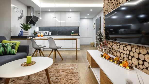 Una cocina moderna con armarios blancos, un comedor con mesa y sillas blancas, y una sala de estar con sofá y televisor.