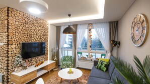 Una sala de estar moderna con televisor, pared de troncos de madera, sillón verde y un reloj grande.