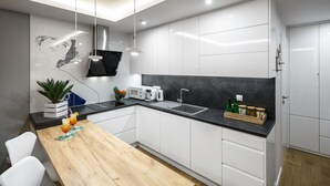 Una cocina moderna con armarios blancos, encimera negra, mesa de comedor de madera y una lámpara colgante negra.