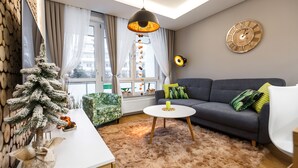 Una sala de estar moderna con un sofá gris, una mesa de centro blanca, una alfombra mullida, un árbol de Navidad decorativo y un reloj de pared grande.