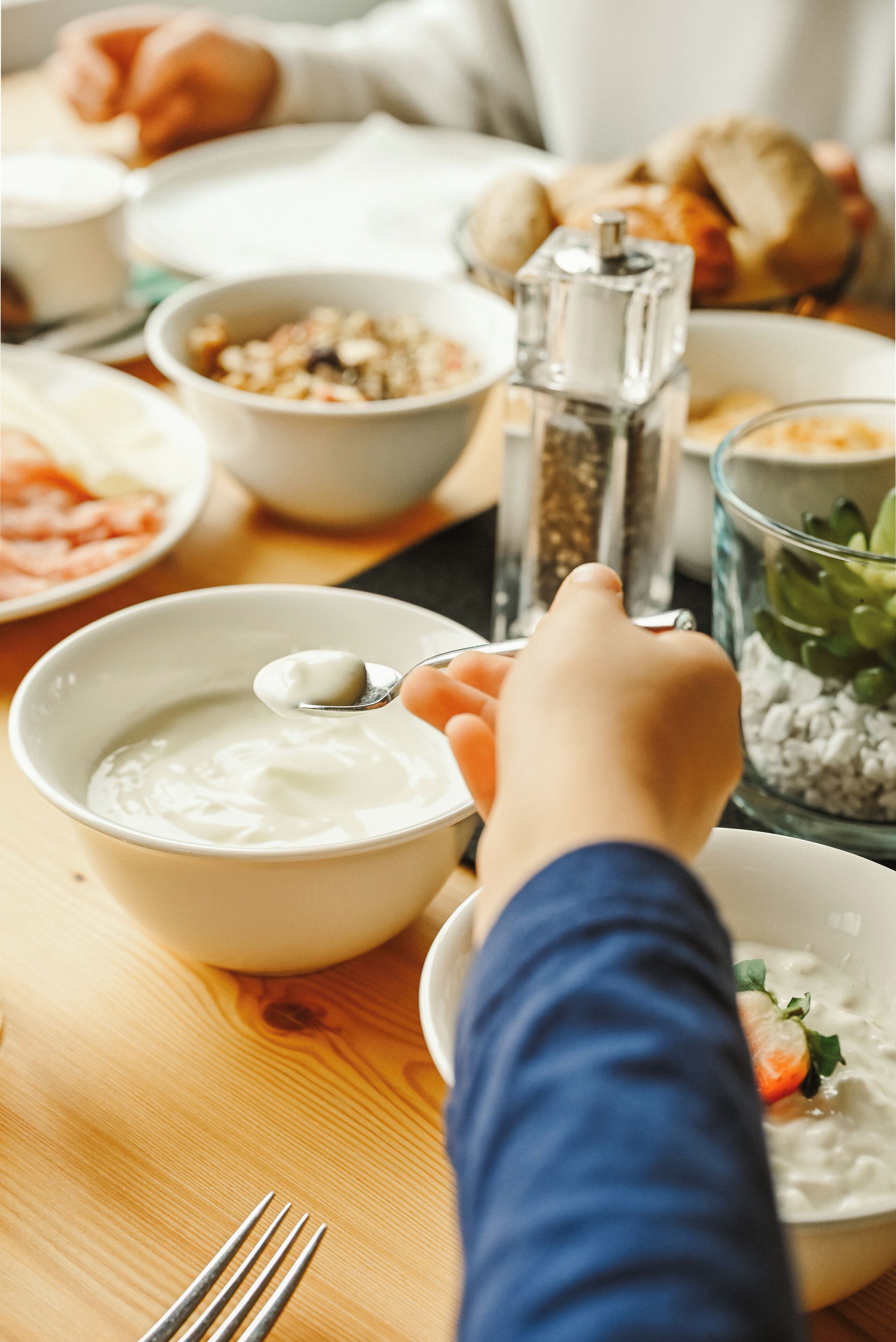 A dining table with various food items, including a bowl of yogurt, a plate with a carrot, and a pepper grinder.