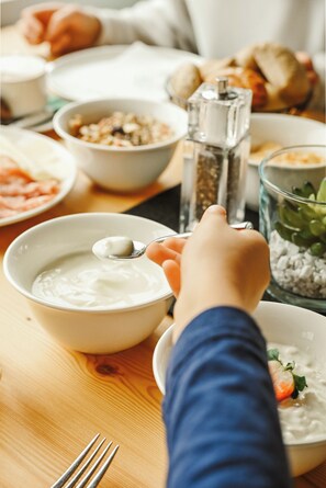A dining table with various food items, including a bowl of yogurt, a plate with a carrot, and a pepper grinder. - Das Mühlwald Quality Time Family Resort (Naz Sciaves)