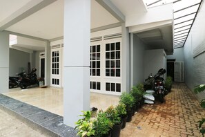 A covered parking area with two motorcycles parked, a row of potted plants, and a tiled floor. - MK House Tendean (Jakarta)
