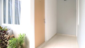 A hallway with a wooden door, a potted plant, and a window with curtains. - MK House Tendean (Jakarta)