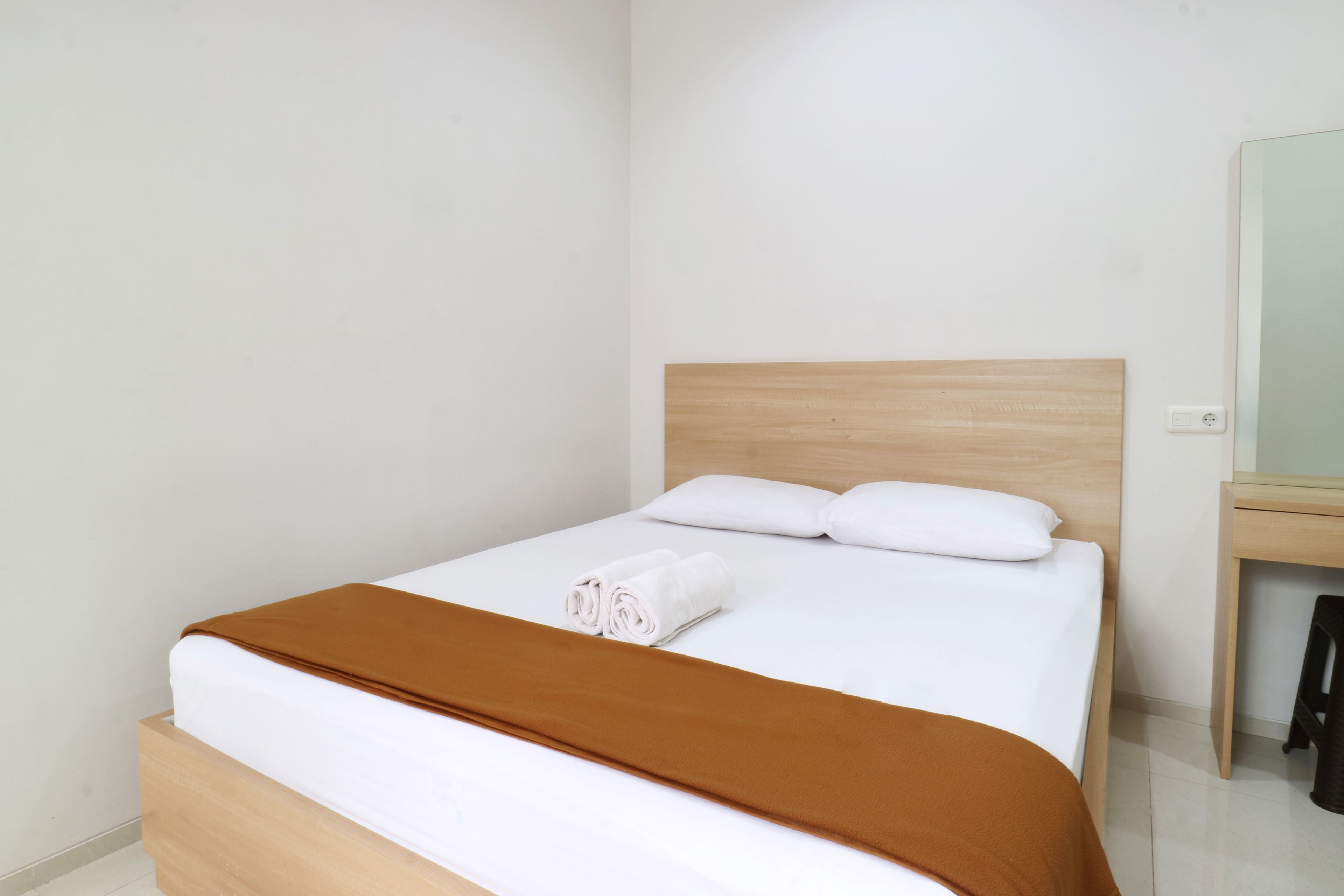 Una cama bien hecha con un edredón marrón y dos almohadas blancas, un cabecero de madera y una mesita de noche de madera con una lámpara.