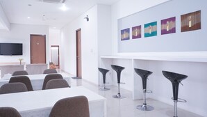 A modern conference room with a long table, several chairs, and a bar area with stools. - MK House Tendean (Jakarta)