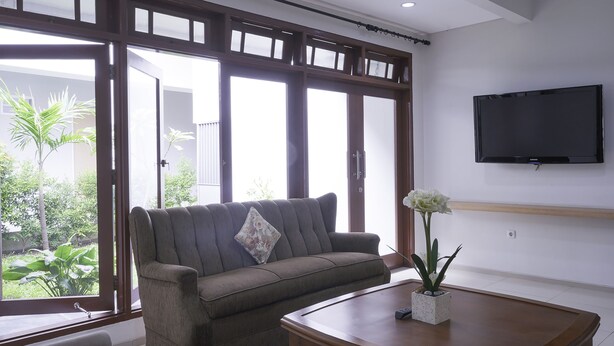 A living room with a sofa, a coffee table, and a TV mounted on the wall. - MK House Tendean (Jakarta)