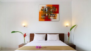 A hotel room with a large bed, white bedding, a wooden headboard, two bedside tables with lamps, and a wall-mounted artwork. - Pondok Jempiring Kuta Bali (Kuta)