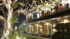 A hotel with a well-lit facade, multiple balconies, and a garden area with plants and a pathway. - Pondok Jempiring Kuta Bali (Kuta)