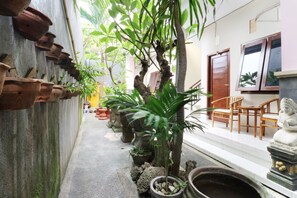 A narrow alley with potted plants, a Buddha statue, and wooden furniture. - Anantaya Home Denpasar (Denpasar)