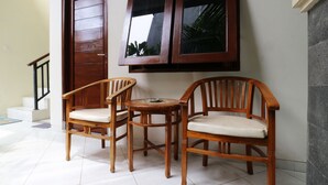 Une pièce avec deux chaises en bois et une petite table, une porte en bois et une fenêtre donnant sur des palmiers.