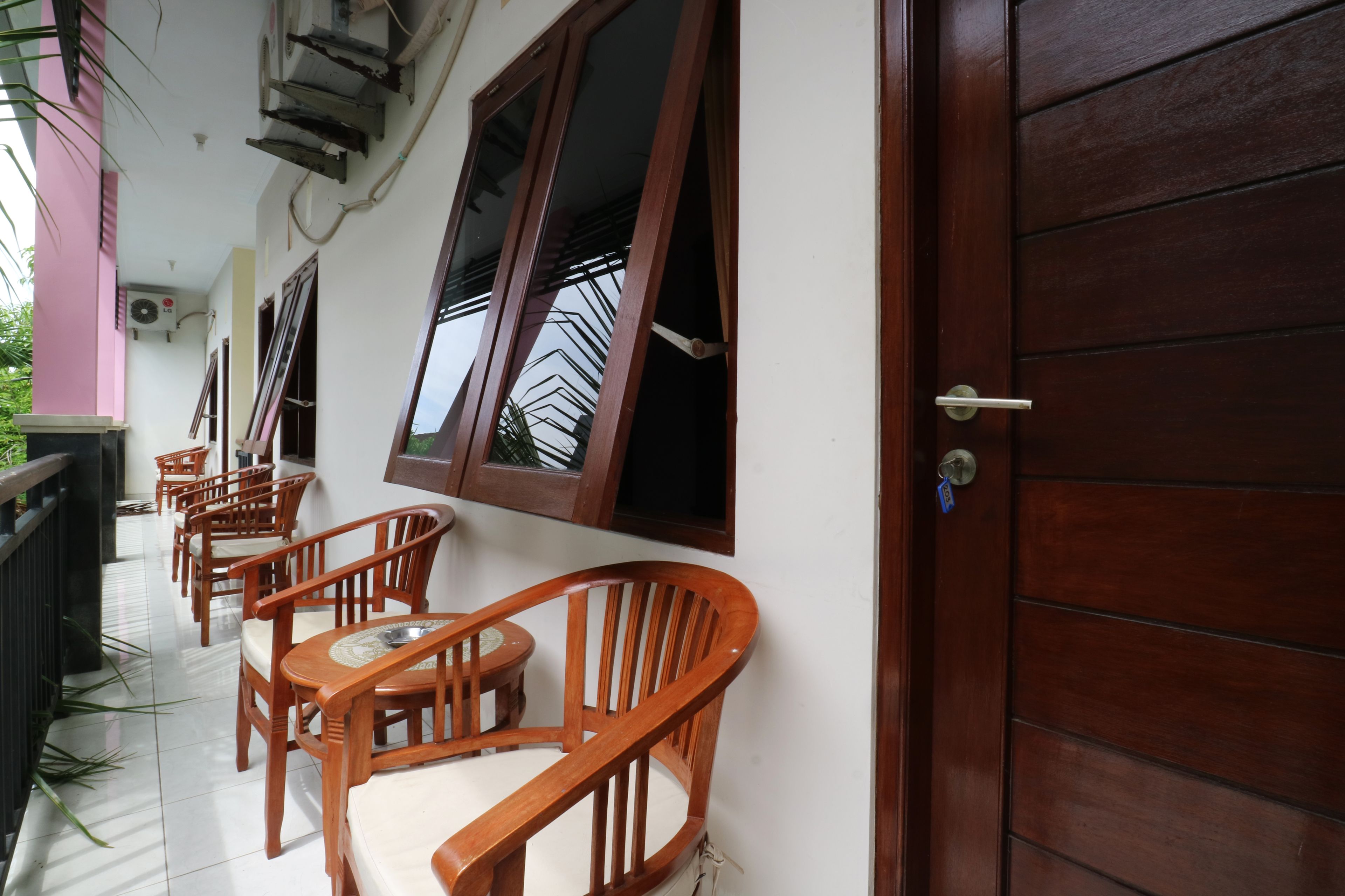 A covered outdoor seating area with wooden chairs and tables, a wooden door, and a window with a metal grill.