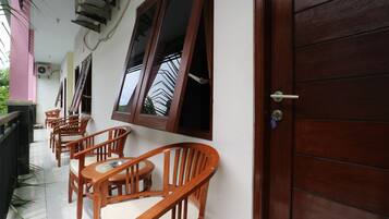 A covered outdoor seating area with wooden chairs and tables, a wooden door, and a window with a metal grill.