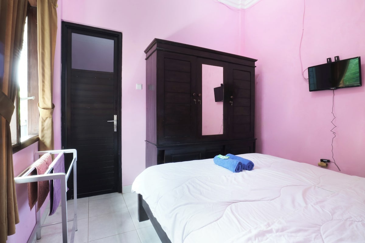 A bedroom with a bed, a wardrobe, a TV mounted on the wall, and a window with curtains.