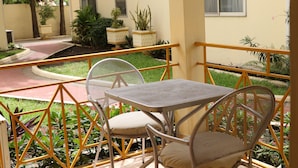 Un patio con mesa y sillas, rodeado de macetas y una barandilla amarilla.