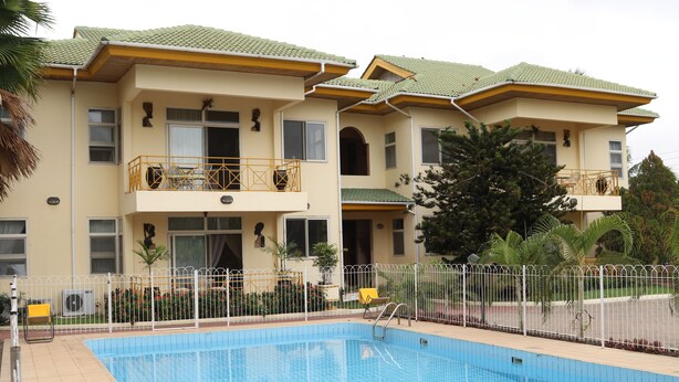 Un edificio de dos plantas con piscina, balcones y un jardín vallado.