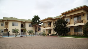Un hotel de varios pisos con un patio empedrado, balcones y palmeras.