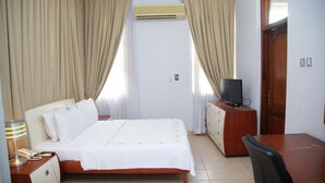 Habitación de hotel con cama, escritorio, televisor, lámpara y aire acondicionado.