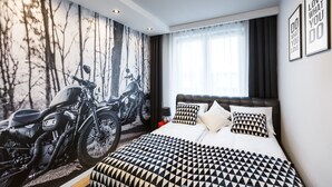 Ein modernes Hotelzimmer mit einem großen Bett, einem Motorrad-Wandbild und Blick ins Freie.