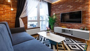 Ein modernes Wohnzimmer mit Backsteinwand, Flachbildfernseher, grauem Sofa, weißem Couchtisch und einem gemusterten Teppich.