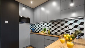 Eine moderne Küche mit grauen Schränken, einer Mikrowelle und einer karierten Spritzschutzwand. Auf der Arbeitsplatte stehen zwei Gläser Orangensaft.