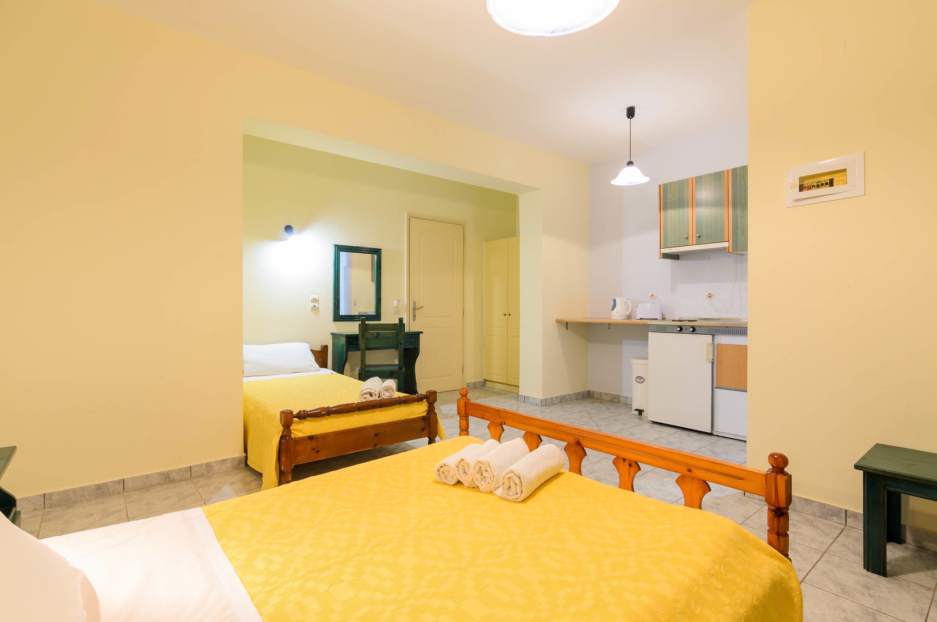 A hotel room with two beds, a small kitchenette, and a bathroom visible through an open door.