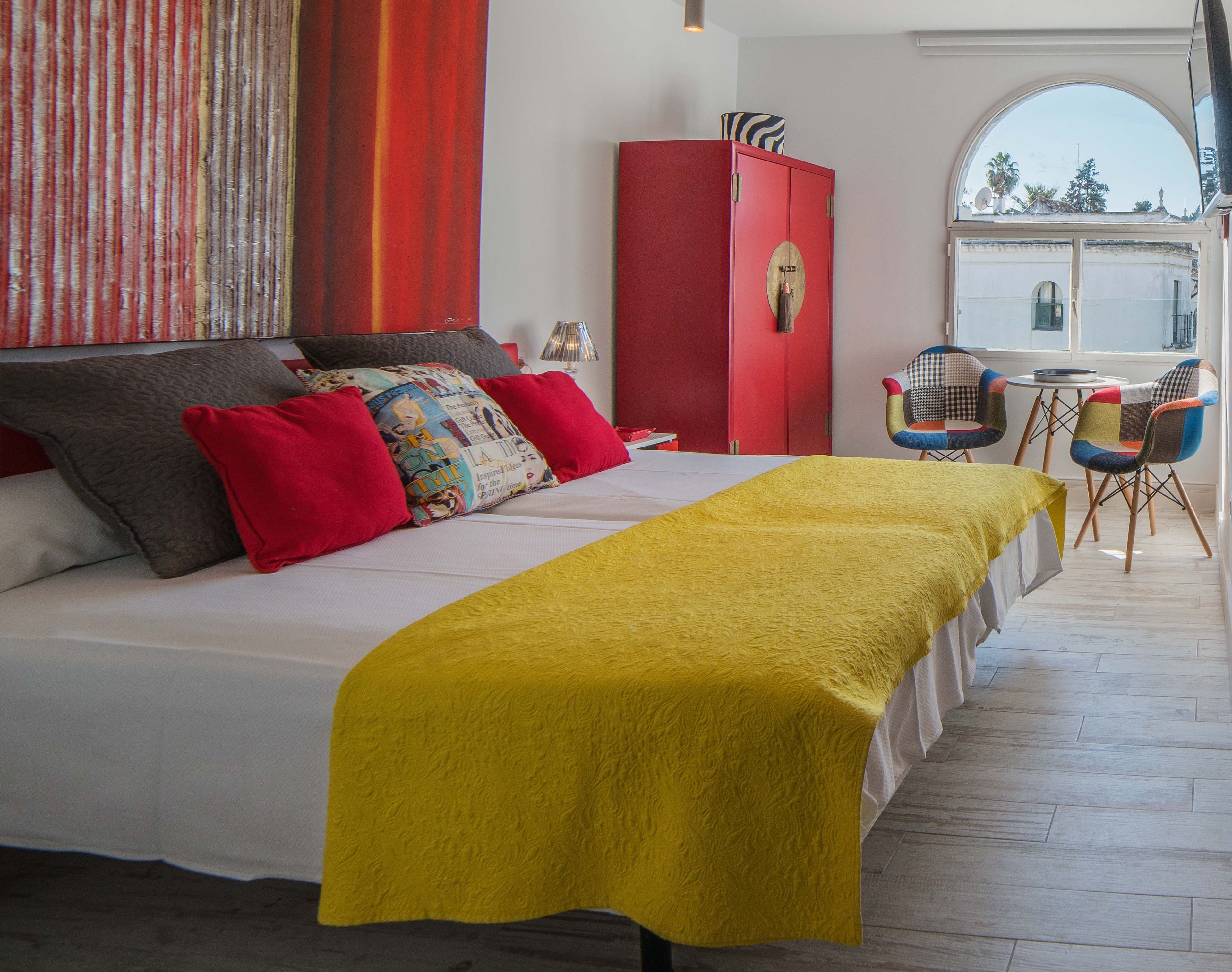 Ein Schlafzimmer mit einem Bett, einem roten Kleiderschrank, einem Fenster mit Aussicht und einem kleinen Tisch mit Stühlen.
