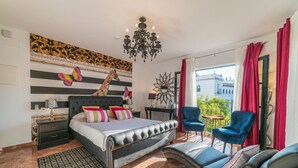 A bedroom with a bed, a nightstand, a dresser, a chandelier, a sofa, and a view of the outside. - Rey Don Pedro Luxury Home (Seville)