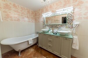 A bathroom with a clawfoot bathtub, a large ornate mirror, and a vanity with two sinks.
