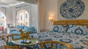 A hotel room with a bed, a small table, and a chair. There are two windows with arched tops. - Rey Don Pedro Luxury Home (Seville)