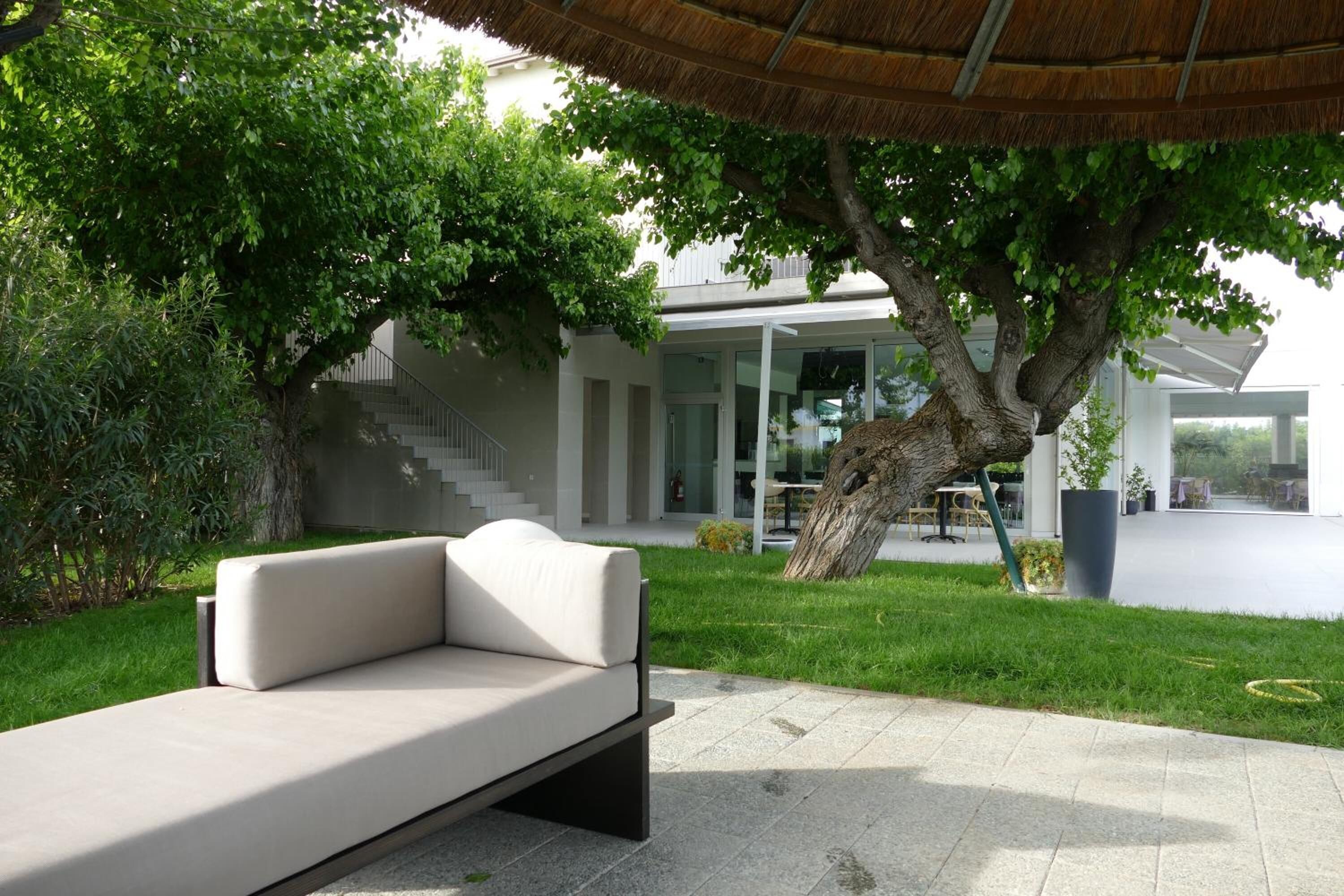 A modern outdoor seating area with a sofa, a tree, and a building with a staircase in the background.