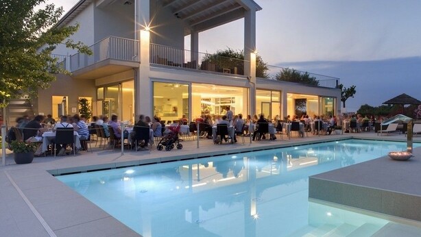 An outdoor pool area with a dining terrace and a building with large windows. - Il Portico (Fano)