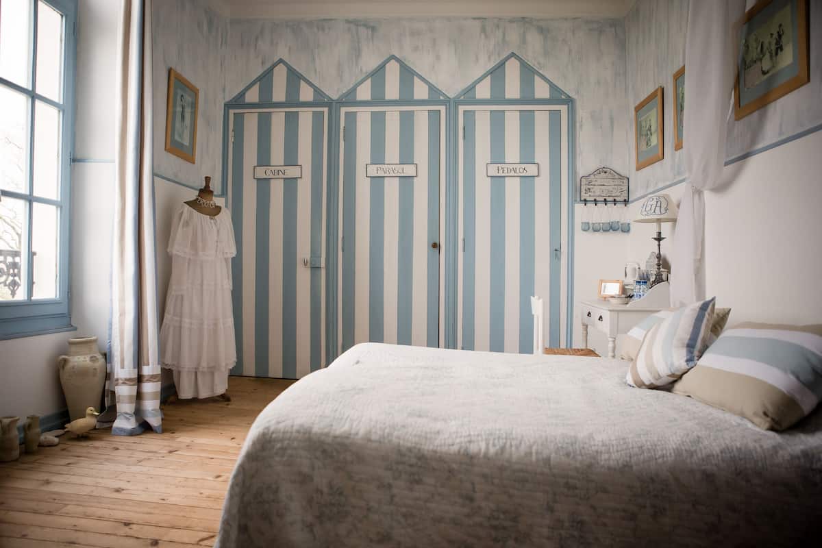 A room with a bed, a dresser, and three striped doors labeled CABNE, PARASOL, and PEDNLOS.