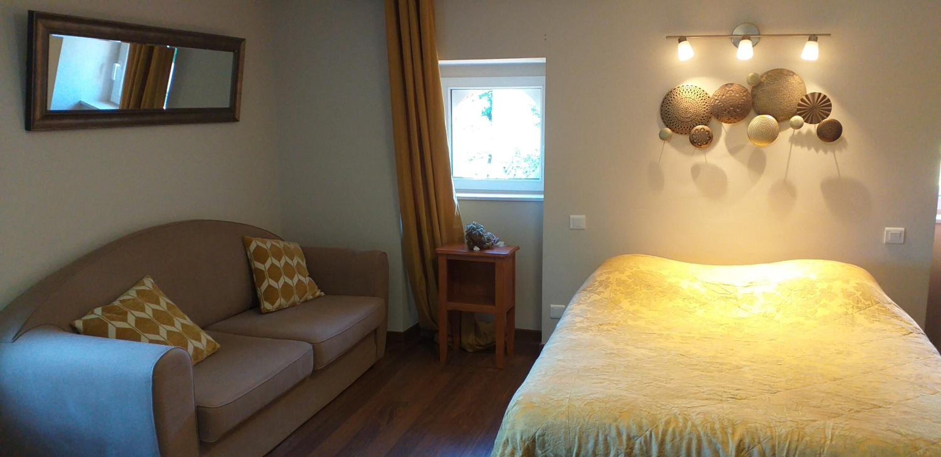 A room with a brown sofa, a bed with a textured blanket, a small wooden table, and wall-mounted decorative items.
