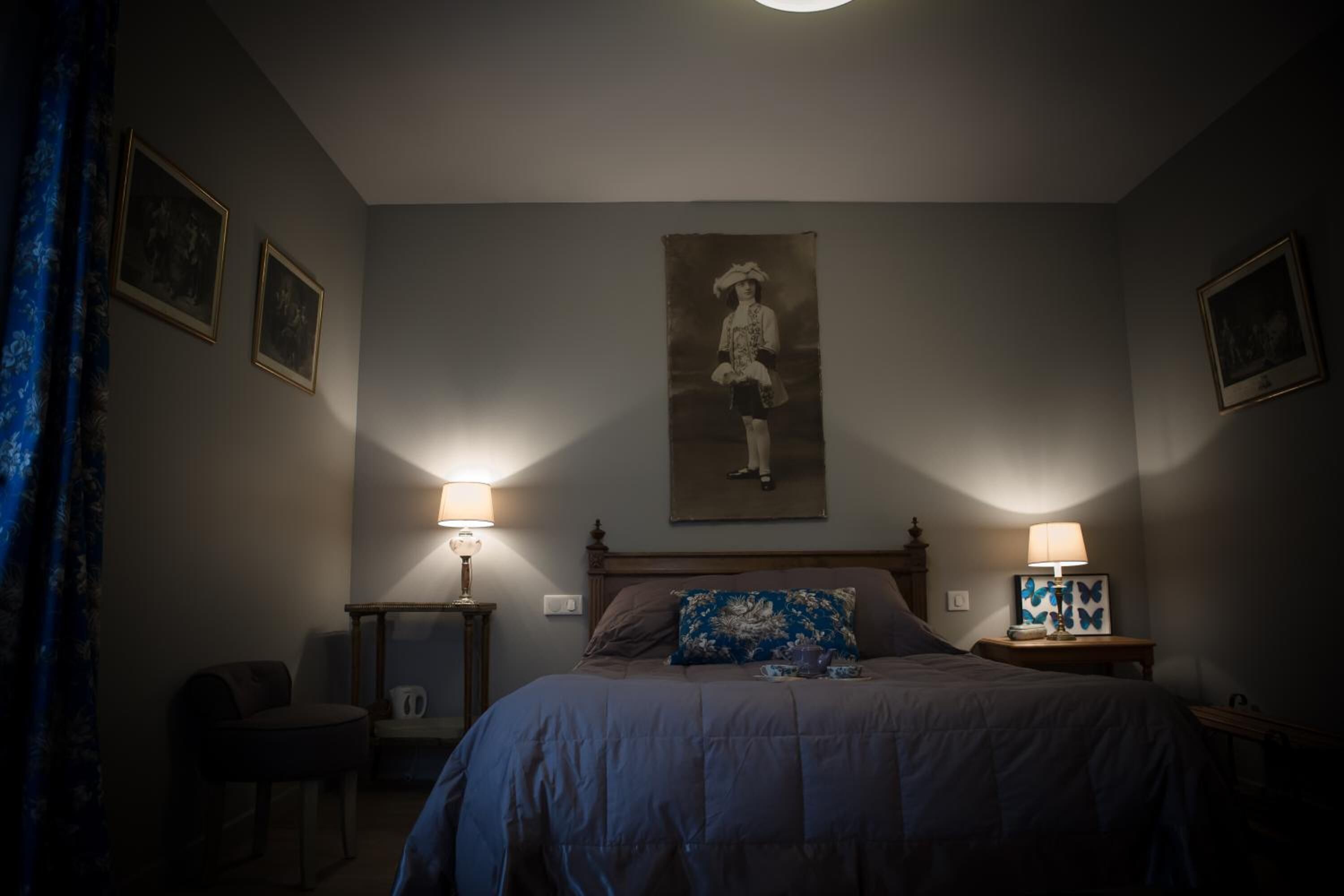 A bedroom with a bed, two bedside tables with lamps, a chair, and framed pictures on the walls.