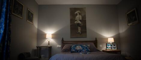 A bedroom with a bed, two bedside tables with lamps, a chair, and framed pictures on the walls.
