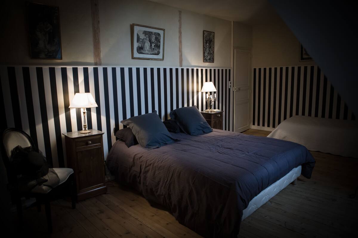 A bedroom with a striped headboard, two bedside tables with lamps, a bed with a blue comforter, and a chair.
