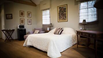 Un dormitorio con una cama grande, un escritorio, una silla, una mesita y una ventana con cortinas.