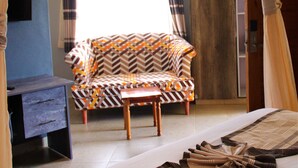 Quarto com sofá estampado, uma pequena mesa de madeira, televisão em um suporte e cama com colcha estampada.