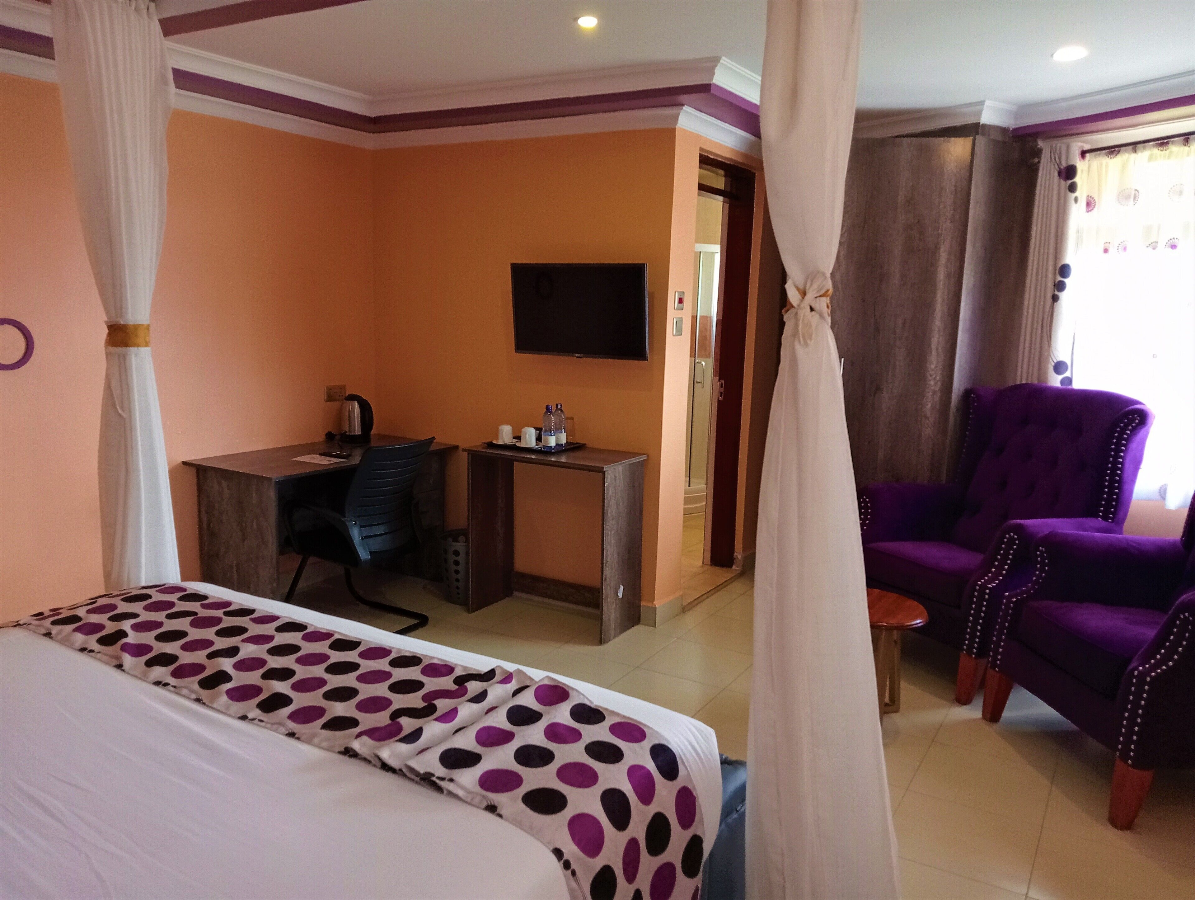 A hotel room with a bed, a desk, a purple armchair, and a television.
