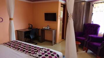 A hotel room with a bed, a desk, a purple armchair, and a television.